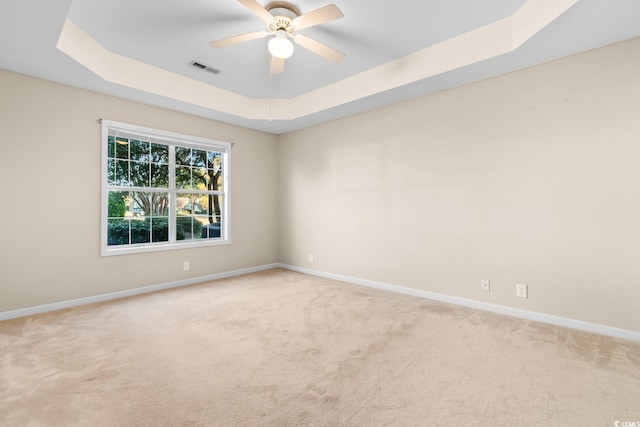 empty room with a raised ceiling, ceiling fan, and light colored carpet