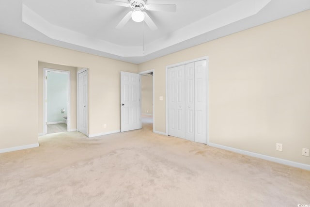 unfurnished bedroom with ceiling fan, a raised ceiling, light carpet, and ensuite bath