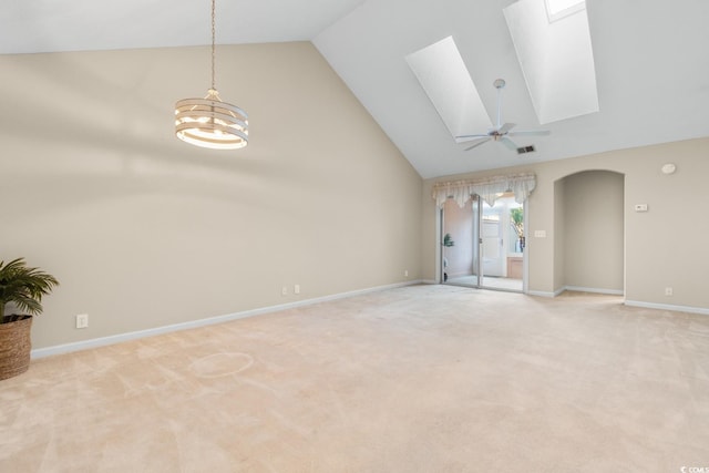 unfurnished living room with a skylight, high vaulted ceiling, light colored carpet, and ceiling fan with notable chandelier