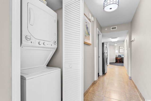 laundry room featuring stacked washing maching and dryer and light tile patterned flooring