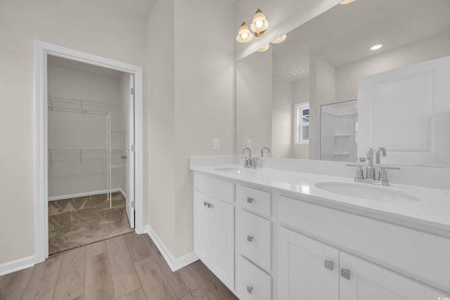 bathroom with wood finished floors, double vanity, a spacious closet, baseboards, and recessed lighting