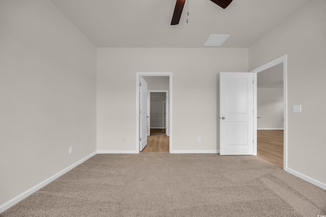 unfurnished bedroom featuring carpet, baseboards, a walk in closet, and a ceiling fan