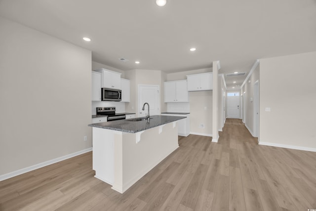 kitchen with appliances with stainless steel finishes, a sink, white cabinets, an island with sink, and baseboards