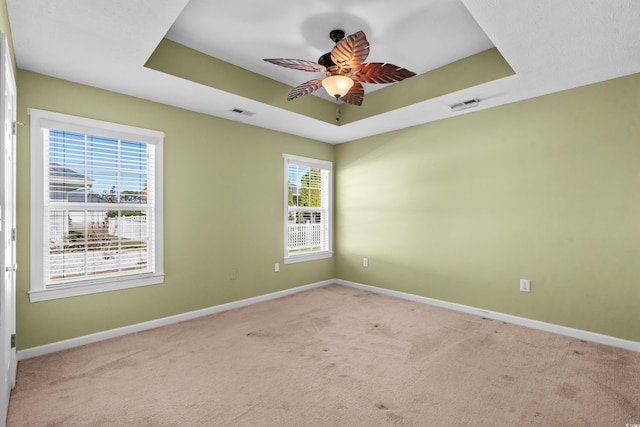 spare room with a raised ceiling, light carpet, and ceiling fan