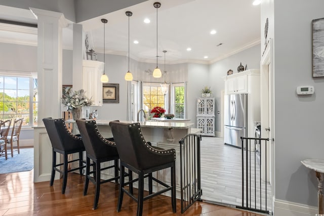 kitchen featuring a kitchen bar, stainless steel fridge, decorative light fixtures, hardwood / wood-style flooring, and white cabinets