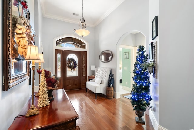 entryway featuring wood-type flooring, crown molding, and a high ceiling