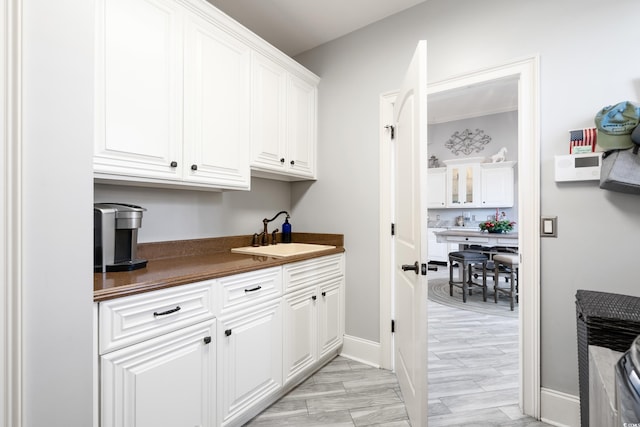 bar with light wood-type flooring, white cabinetry, and sink