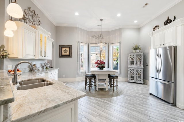 kitchen with light stone countertops, stainless steel fridge, sink, light hardwood / wood-style flooring, and hanging light fixtures