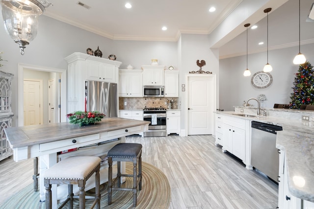 kitchen with light wood-type flooring, light stone counters, ornamental molding, stainless steel appliances, and white cabinets