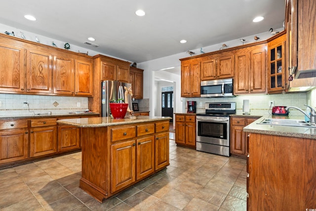 kitchen featuring light stone countertops, sink, backsplash, a kitchen island, and appliances with stainless steel finishes