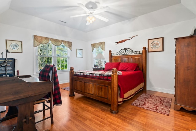 bedroom with ceiling fan, light hardwood / wood-style floors, and a tray ceiling