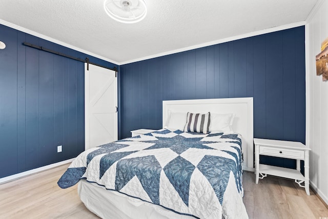 bedroom featuring ornamental molding, wood-type flooring, a barn door, and a textured ceiling