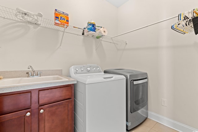 clothes washing area with washer and clothes dryer, light tile patterned flooring, cabinets, and sink