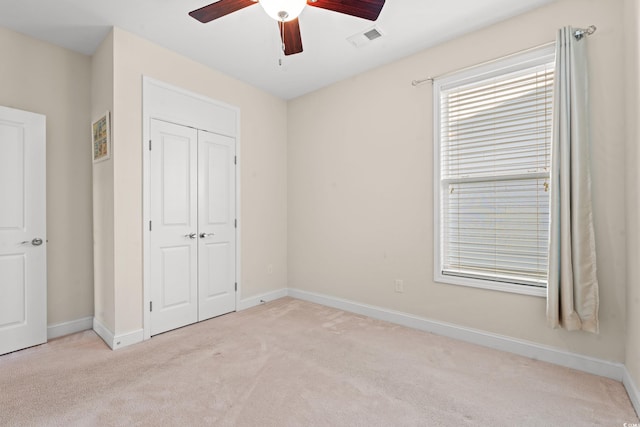 unfurnished bedroom with a closet, light colored carpet, and ceiling fan