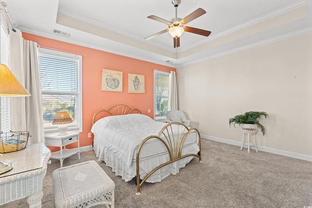 carpeted bedroom with a raised ceiling, multiple windows, ceiling fan, and ornamental molding