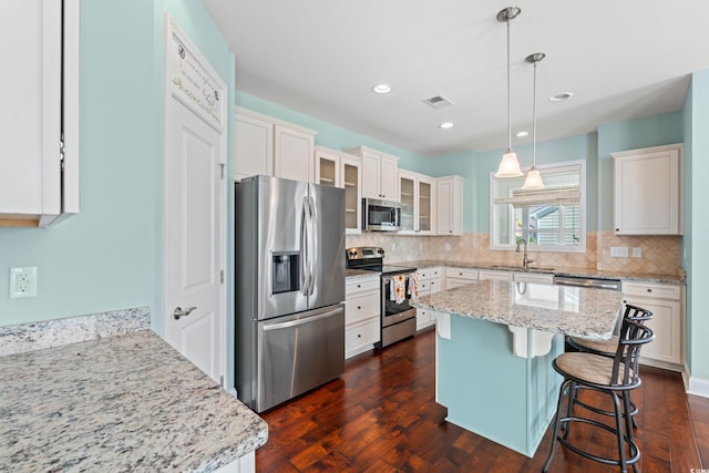 kitchen with light stone countertops, appliances with stainless steel finishes, white cabinets, a kitchen island, and hanging light fixtures