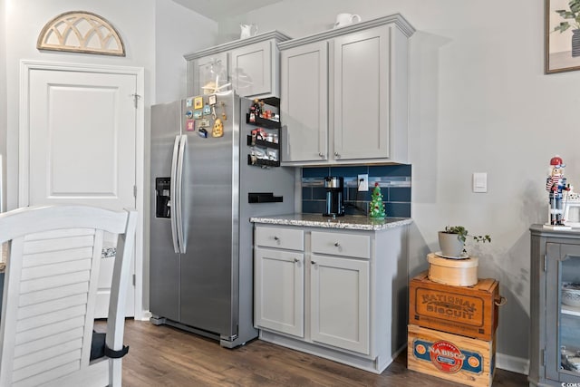 kitchen with gray cabinetry, stainless steel fridge, light stone countertops, and dark wood-type flooring