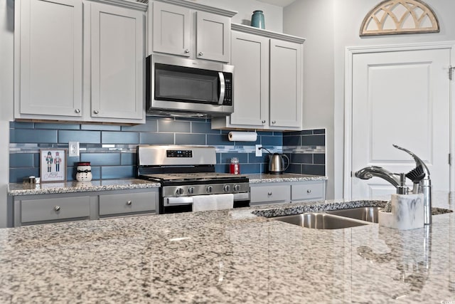 kitchen with appliances with stainless steel finishes, backsplash, light stone counters, gray cabinetry, and sink