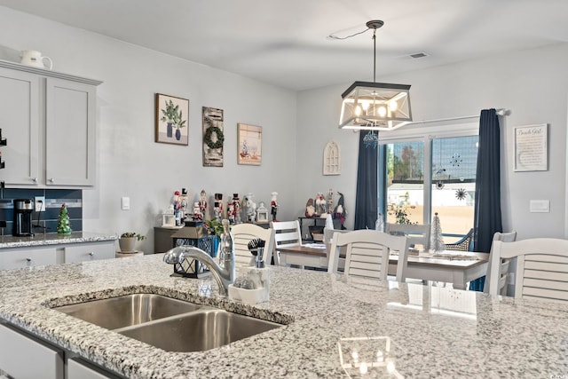 kitchen featuring light stone countertops, sink, pendant lighting, and an inviting chandelier