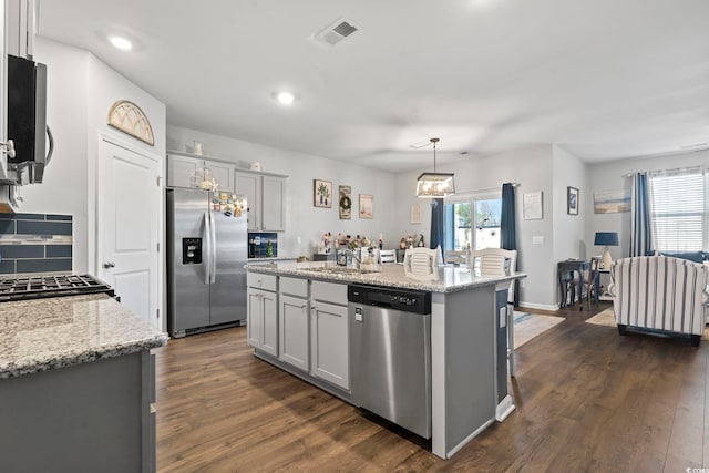 kitchen with gray cabinetry, stainless steel appliances, dark hardwood / wood-style floors, an island with sink, and decorative light fixtures