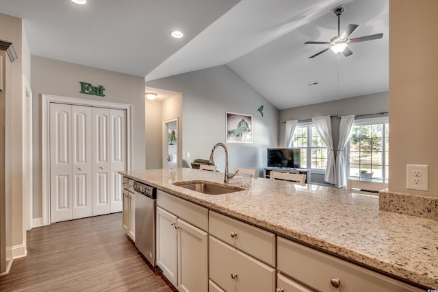 kitchen featuring sink, vaulted ceiling, stainless steel dishwasher, light hardwood / wood-style floors, and light stone counters