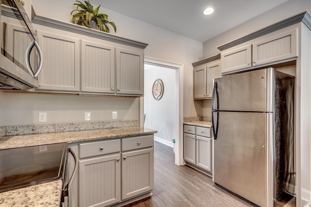 kitchen with gray cabinetry, light stone countertops, hardwood / wood-style floors, and appliances with stainless steel finishes