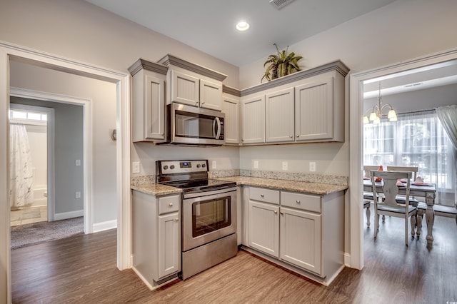 kitchen with light stone countertops, an inviting chandelier, light hardwood / wood-style flooring, gray cabinets, and appliances with stainless steel finishes