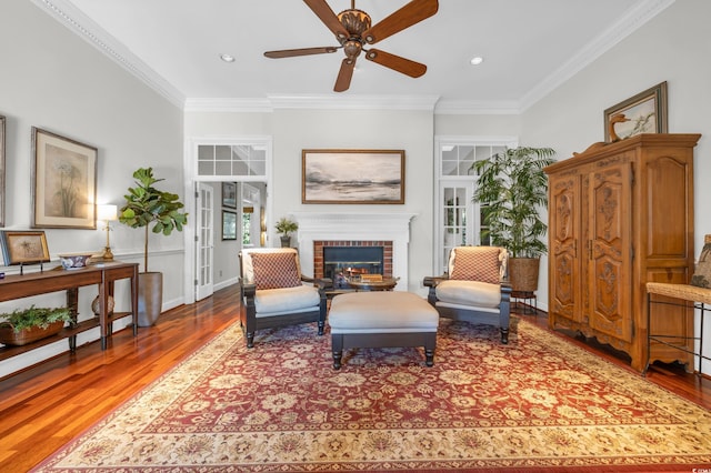 living area with a fireplace, crown molding, hardwood / wood-style floors, and ceiling fan