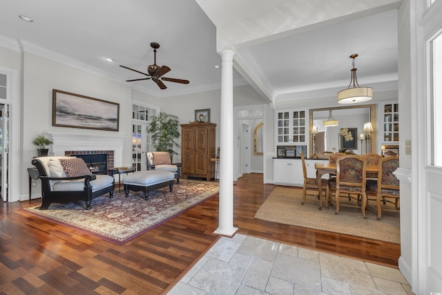 living room featuring ornate columns, ceiling fan, light hardwood / wood-style floors, and a brick fireplace