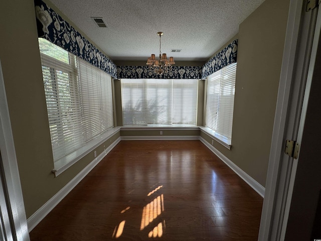 unfurnished dining area with dark hardwood / wood-style flooring, plenty of natural light, a textured ceiling, and an inviting chandelier