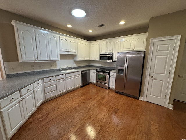 kitchen with white cabinets, appliances with stainless steel finishes, sink, and wood-type flooring