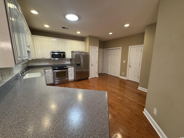 kitchen featuring appliances with stainless steel finishes, a textured ceiling, dark wood-type flooring, sink, and white cabinetry