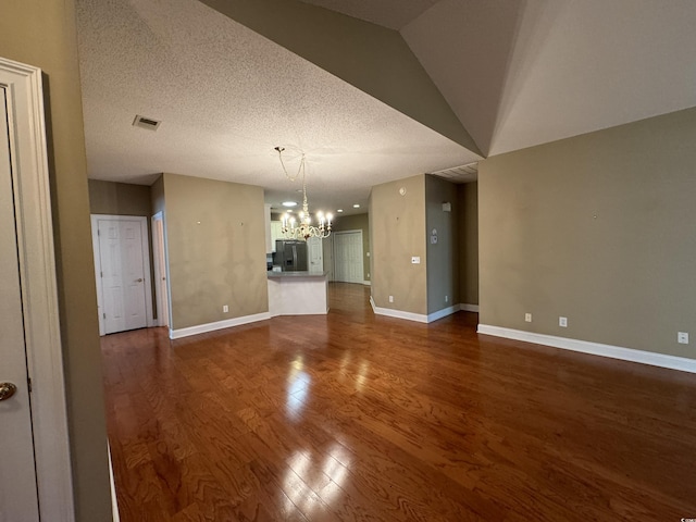 unfurnished living room featuring dark hardwood / wood-style floors, vaulted ceiling, a textured ceiling, and a chandelier