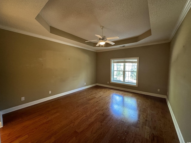 empty room with a textured ceiling, crown molding, dark wood-type flooring, and a tray ceiling