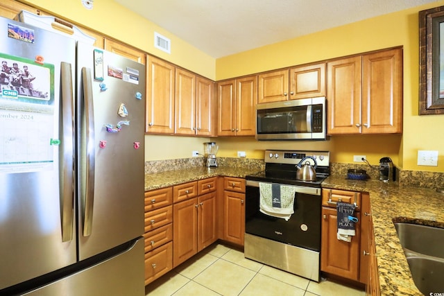 kitchen featuring dark stone countertops, light tile patterned floors, sink, and appliances with stainless steel finishes