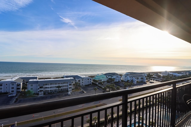 balcony at dusk featuring a water view and a beach view