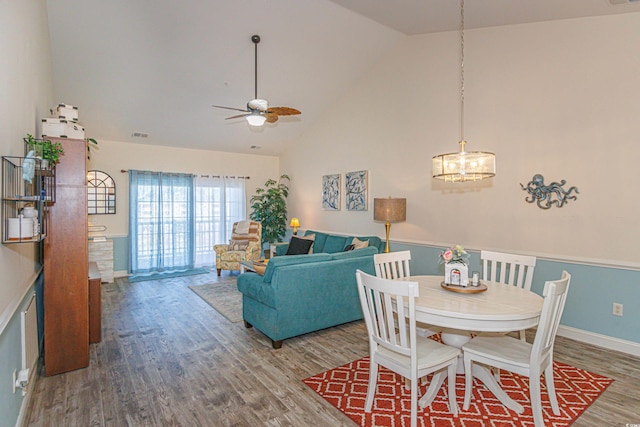 dining room with wood-type flooring, ceiling fan with notable chandelier, and high vaulted ceiling