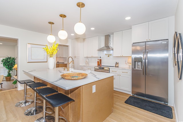 kitchen with light stone counters, stainless steel appliances, wall chimney range hood, light hardwood / wood-style floors, and white cabinetry