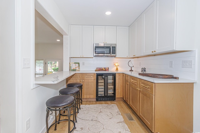 kitchen with a breakfast bar, white cabinetry, kitchen peninsula, and wine cooler