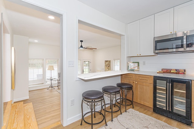 kitchen featuring white cabinets, ceiling fan, light wood-type flooring, kitchen peninsula, and beverage cooler