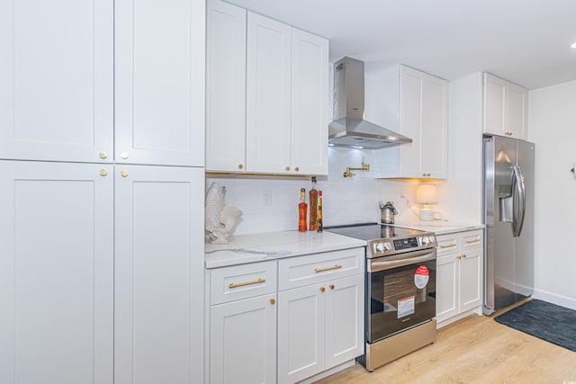 kitchen featuring stainless steel appliances, white cabinetry, light hardwood / wood-style floors, and wall chimney range hood