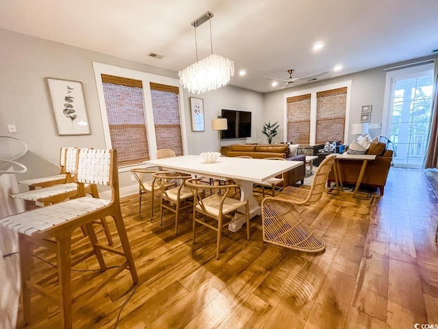 dining area with hardwood / wood-style floors and ceiling fan with notable chandelier