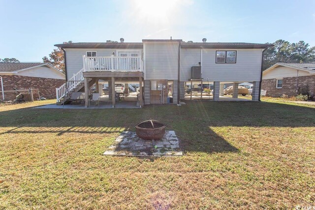 back of house featuring an outdoor fire pit, a wooden deck, and a lawn