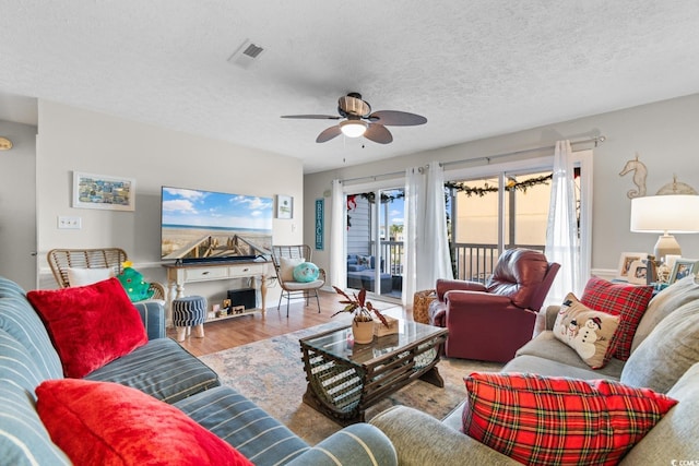 living room featuring ceiling fan, light wood-type flooring, and a textured ceiling