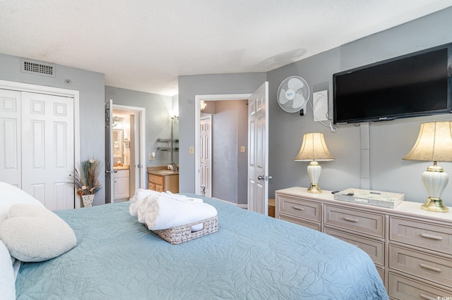 bedroom with a textured ceiling, ensuite bathroom, a closet, and sink