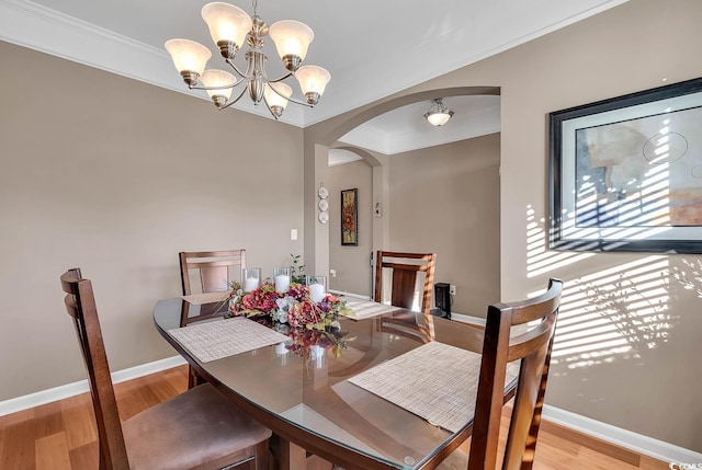 dining area with light wood-type flooring, crown molding, and an inviting chandelier