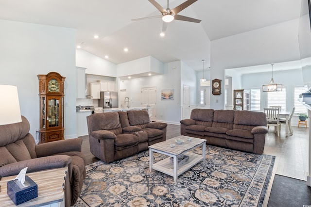 living room with sink, high vaulted ceiling, dark wood-type flooring, and ceiling fan with notable chandelier