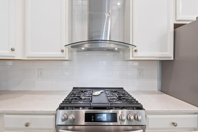 kitchen featuring gas range, white cabinetry, light stone countertops, wall chimney exhaust hood, and backsplash