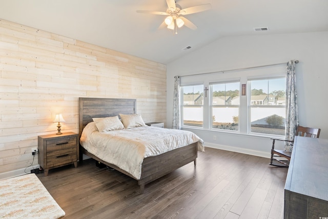 bedroom with dark hardwood / wood-style flooring, vaulted ceiling, ceiling fan, and wooden walls