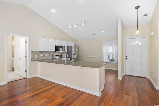 kitchen featuring kitchen peninsula, dark stone counters, stainless steel appliances, decorative light fixtures, and white cabinets